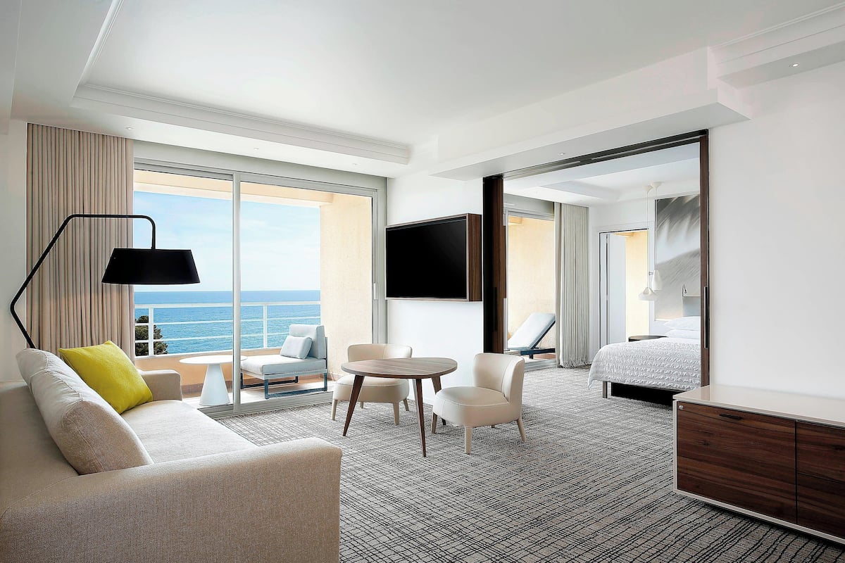 A modern hotel room with a sofa, chairs, a small table, a TV, and a bed.
