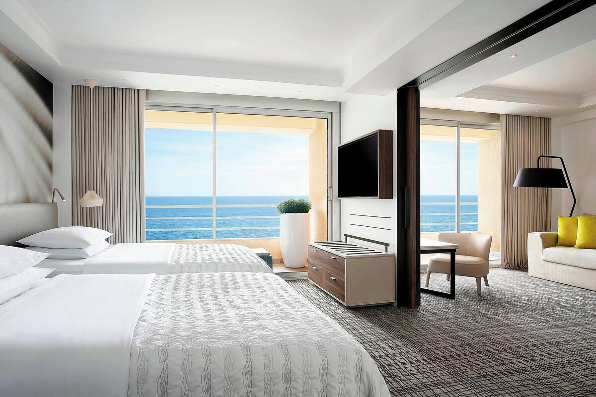 A hotel room with two beds, a TV, a desk, a chair, and a sofa.
