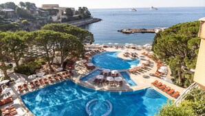 A resort pool with multiple sunbathing areas, a view of the sea, and a dock with boats. - Le Meridien Beach Plaza (Monaco)