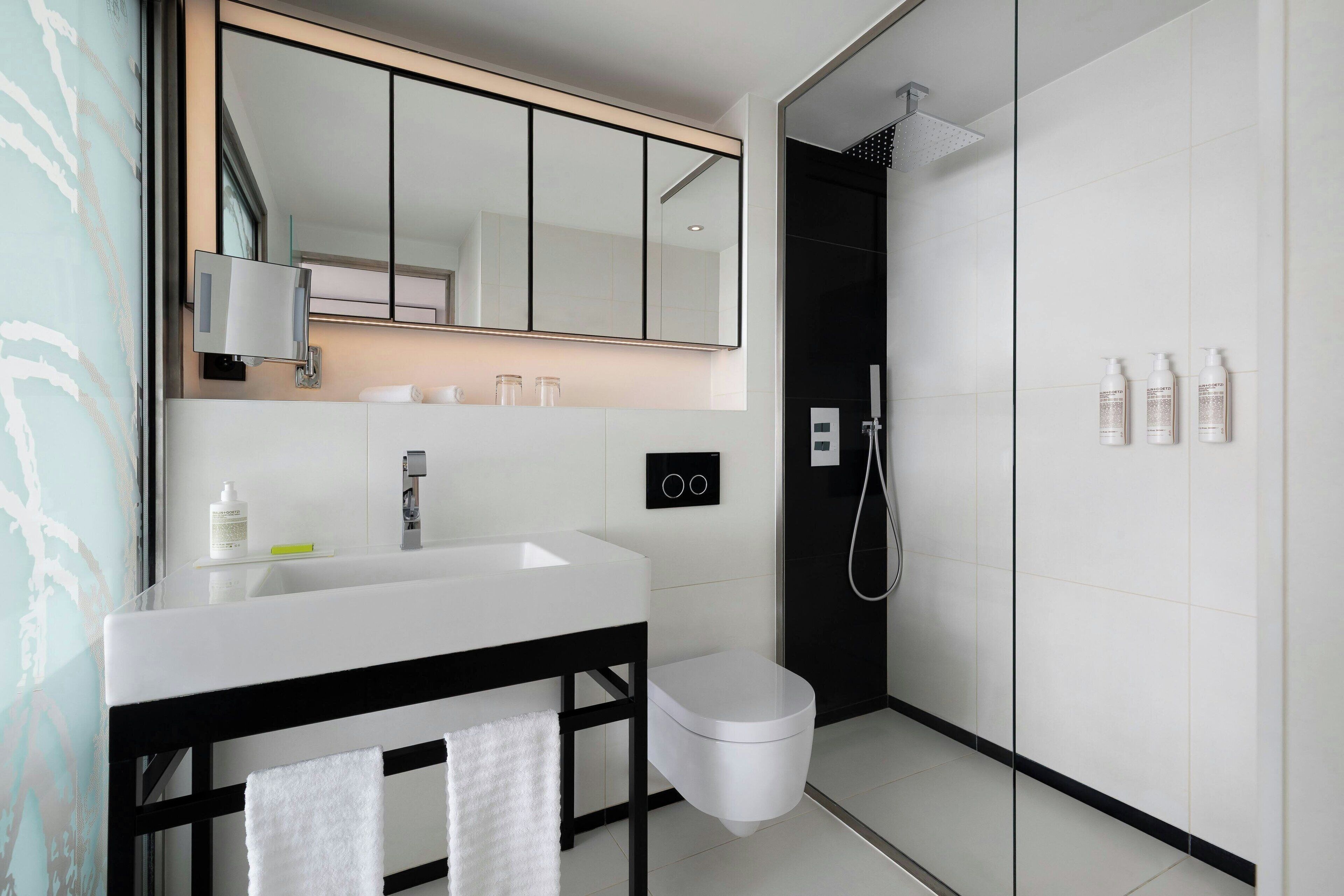 Un bagno moderno con un lavandino bianco, un mobile bagno nero, un water e una cabina doccia in vetro.