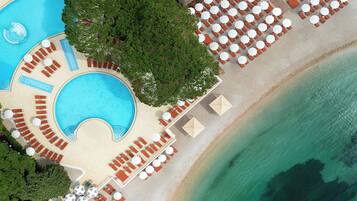 An aerial view of a resort with a swimming pool, beachside lounge areas, and umbrellas.