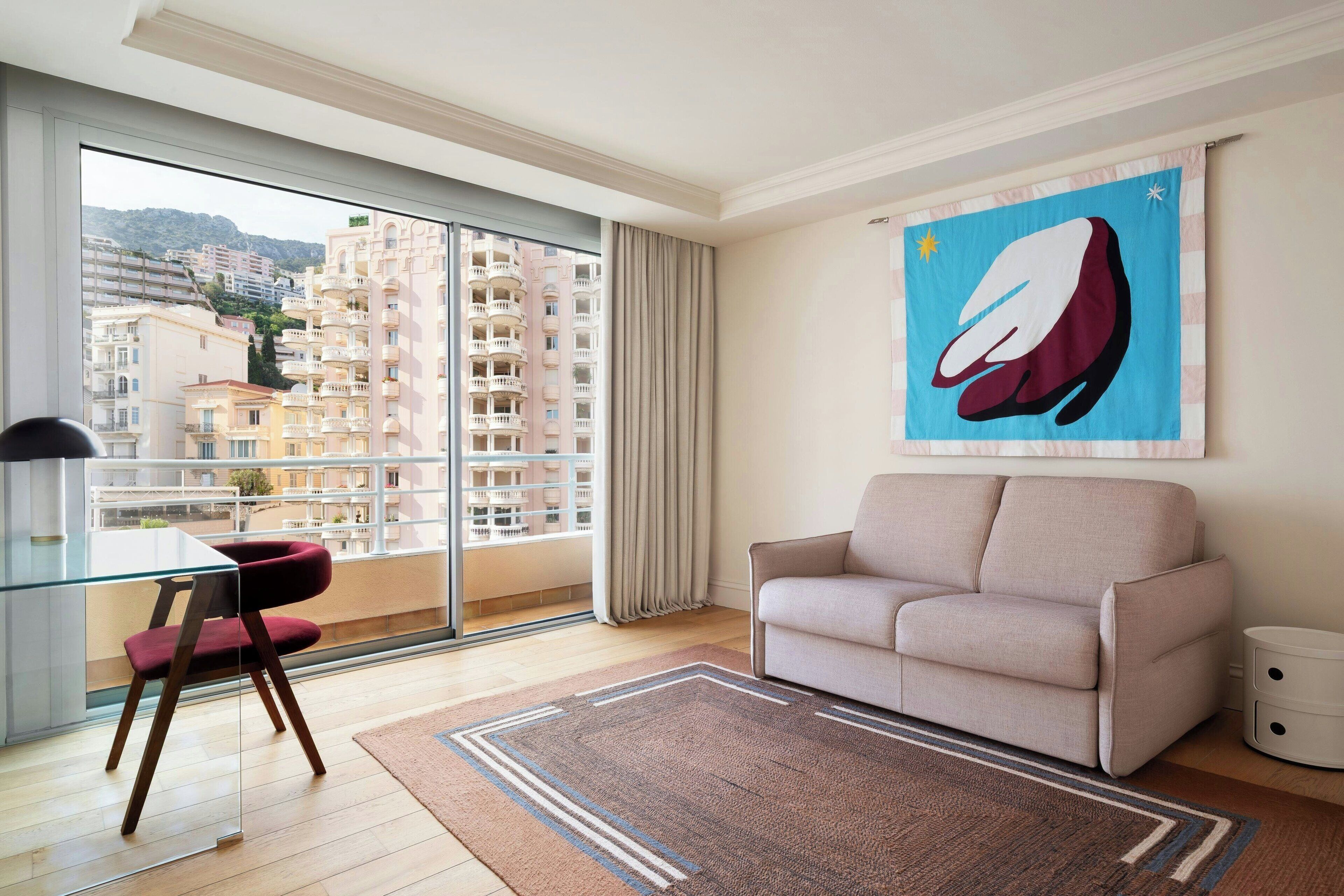 Un salón moderno con una mesa de comedor de vidrio, una silla roja, un sofá beige y un cuadro abstracto grande en la pared.
