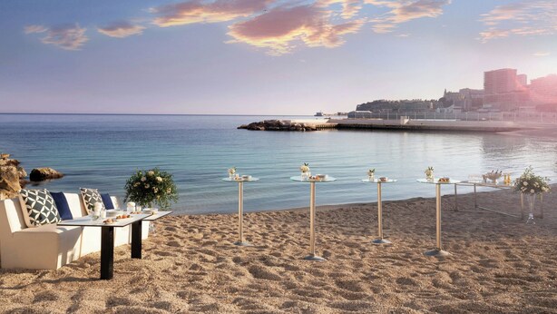 A beachside dining setup with tables and chairs, overlooking the sea and a cityscape in the background. - Le Meridien Beach Plaza (Monaco)