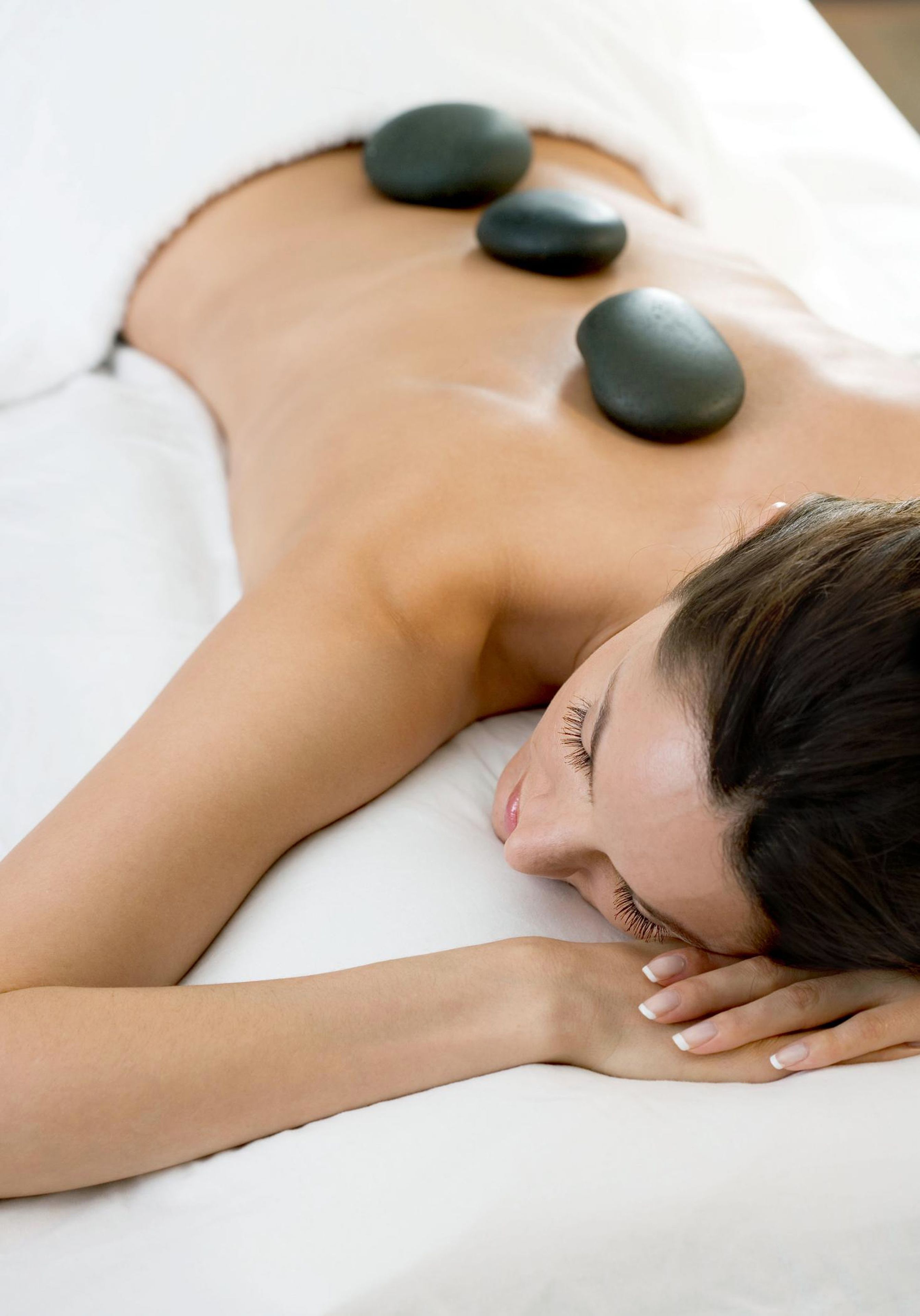 A person lying on a massage table with stones placed on their back.