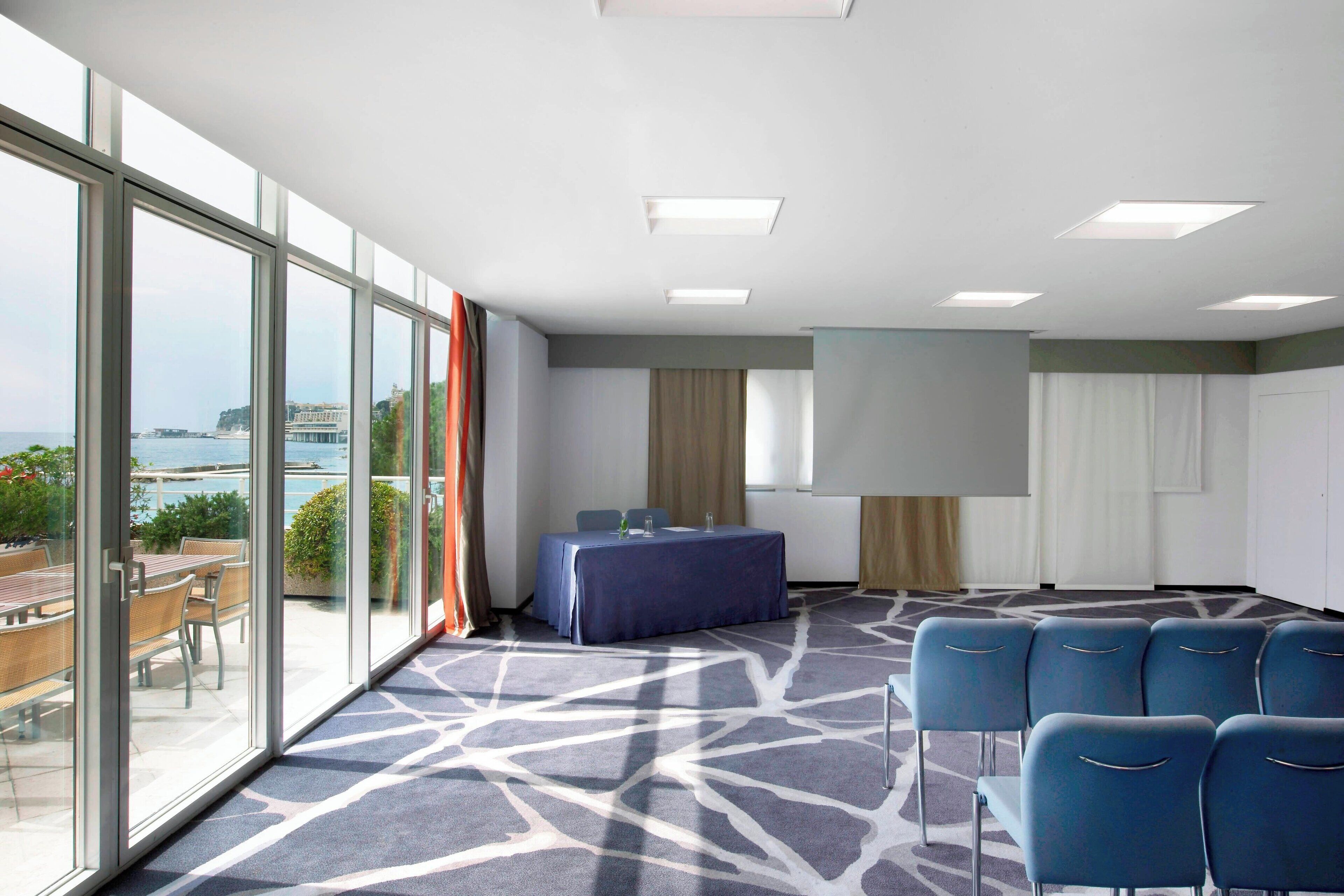 A conference room with a table and chairs, large windows with a view, and a patterned carpet.