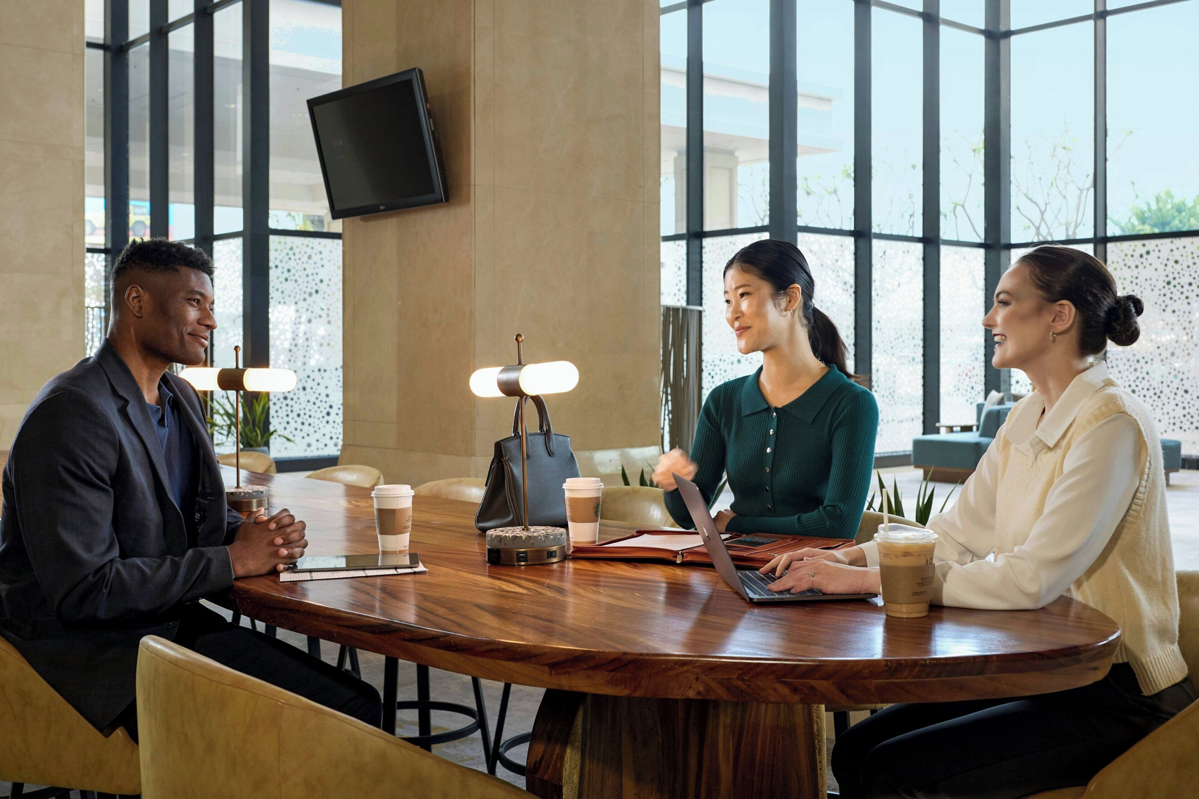 A meeting room with a round table, chairs, a laptop, a coffee cup, a handbag, and a television on the wall.