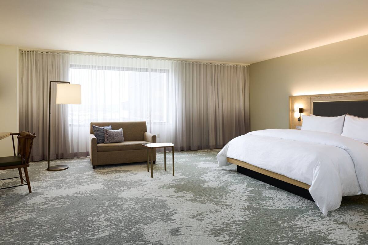 Habitación de hotel con una cama grande, un sofá, una mesita y una lámpara de pie.