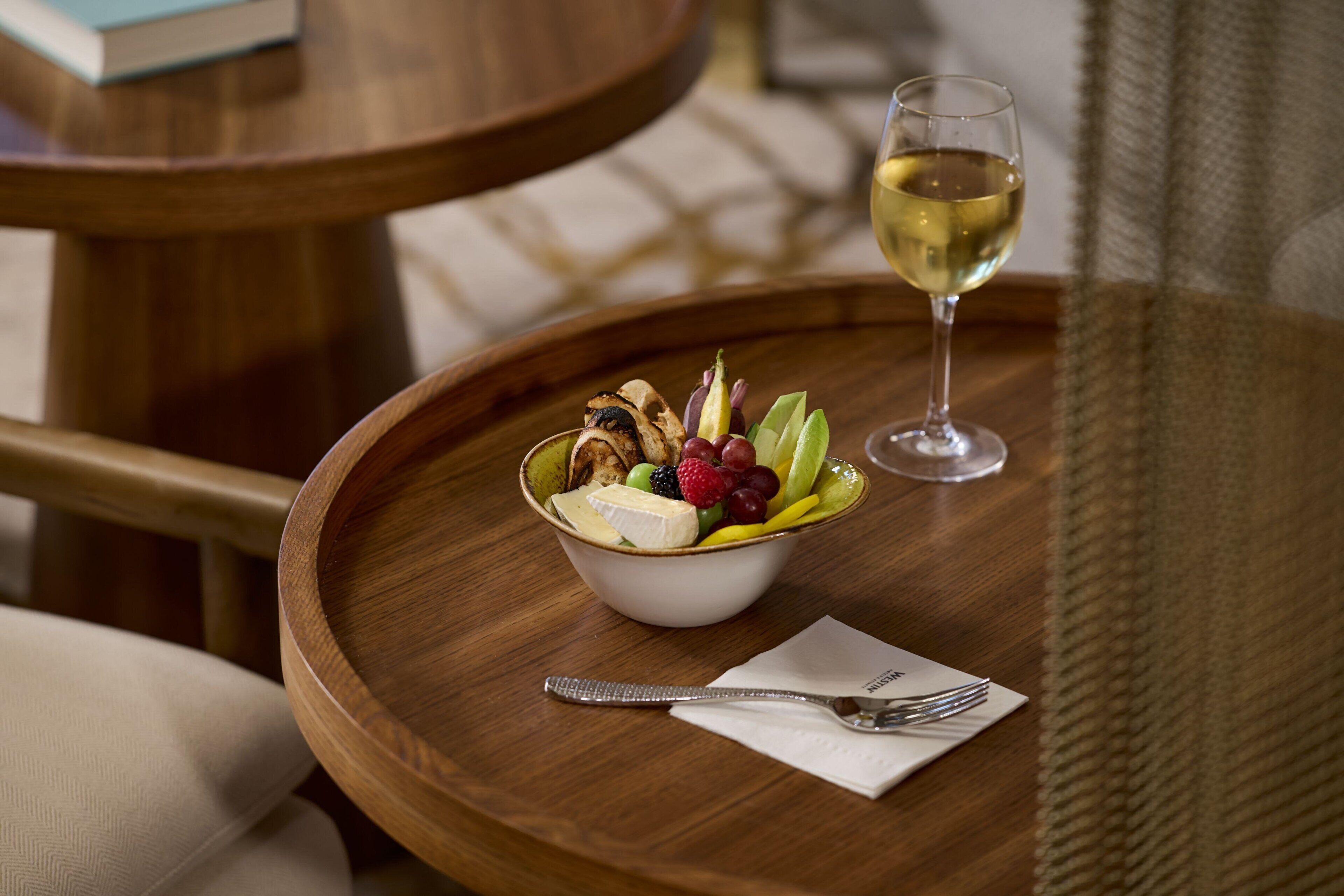 Una mesa de madera con una ensalada de frutas y una copa de vino blanco.