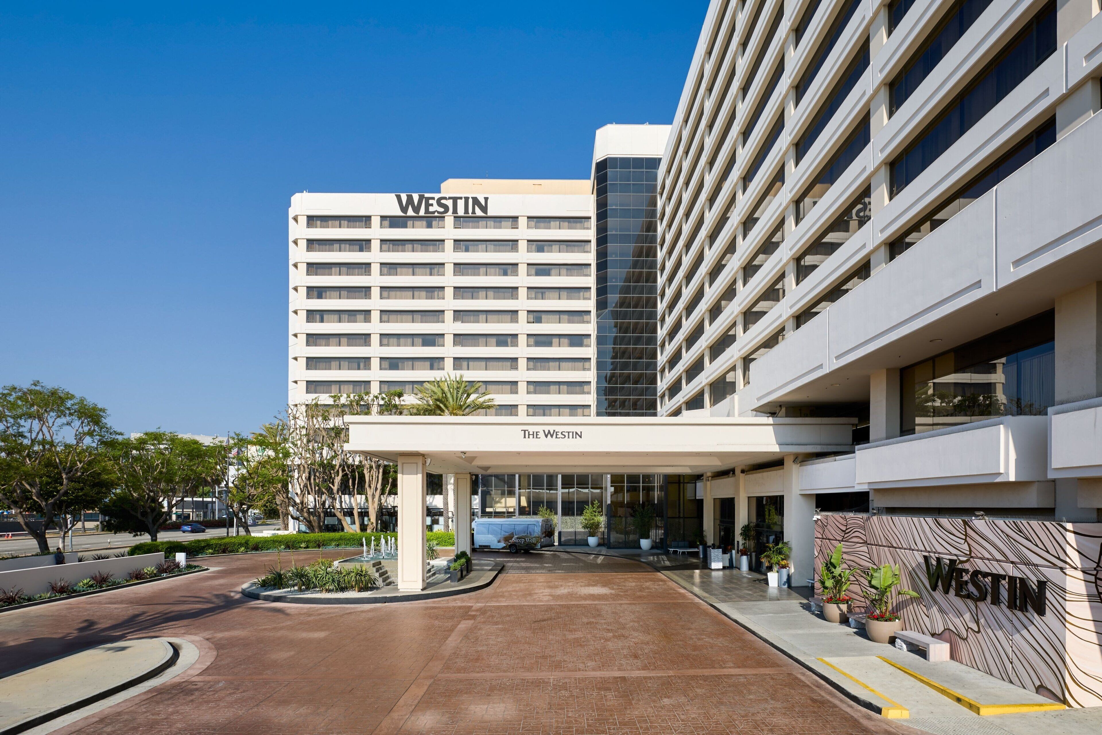 Entrada de hotel con un corredor cubierto, un letrero que dice "WESTIN" y un área de estacionamiento con algunos automóviles.