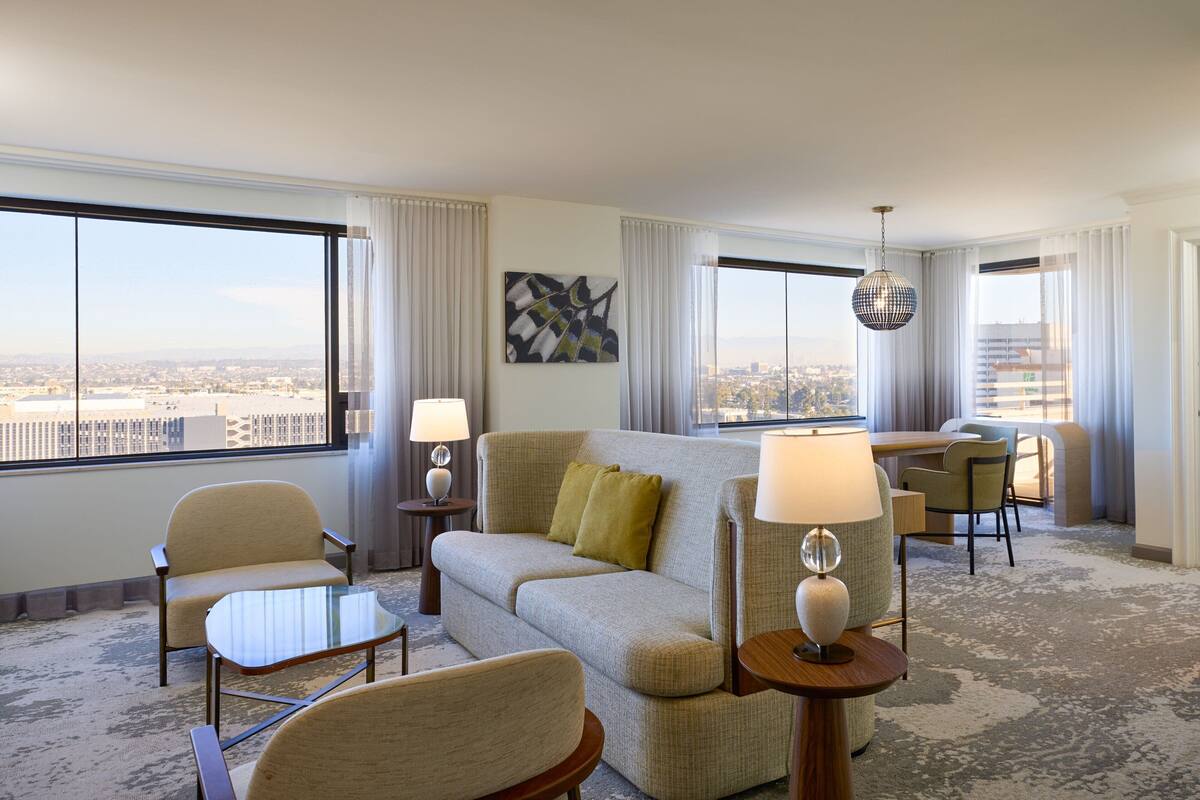 Habitación de hotel con un ventanal grande, un sofá, una mesa de comedor y una lámpara.