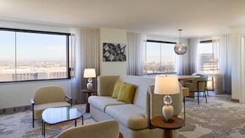 A hotel room with a sofa, chairs, a dining table, and a view of the city.