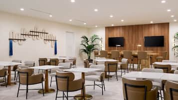 A modern dining area with multiple tables and chairs, a wooden accent wall, and a flat-screen TV mounted above the tables.
