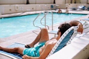 Un hombre descansando en una silla de piscina, con una piscina al fondo.