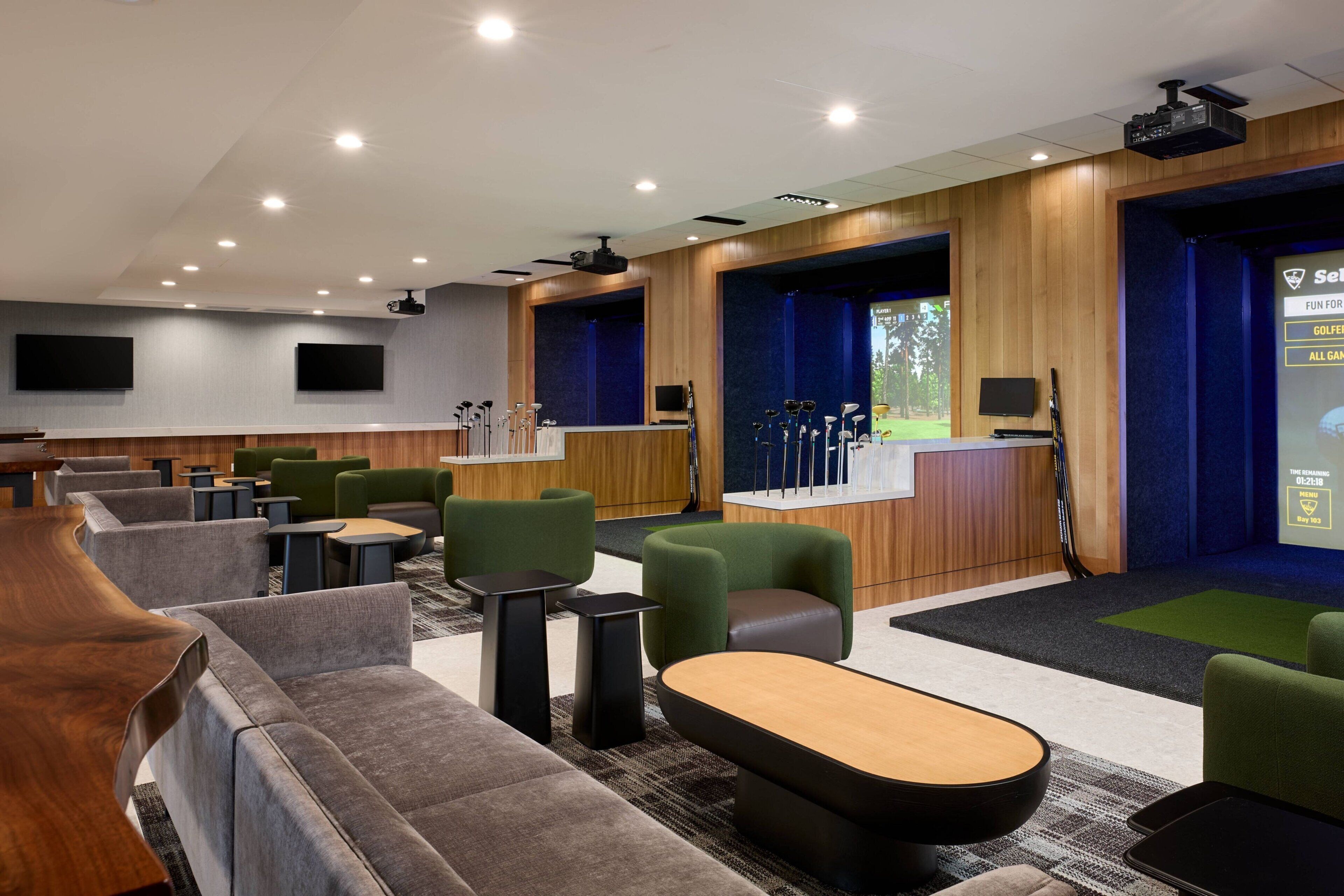 Et moderne loungeområde med flere siddepladser, et billardbord og et projektorskærm, der viser en golfkamp.