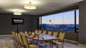 Una sala de conferencias con una gran mesa, sillas, una pantalla de televisión y vistas de la ciudad a través de amplias ventanas.