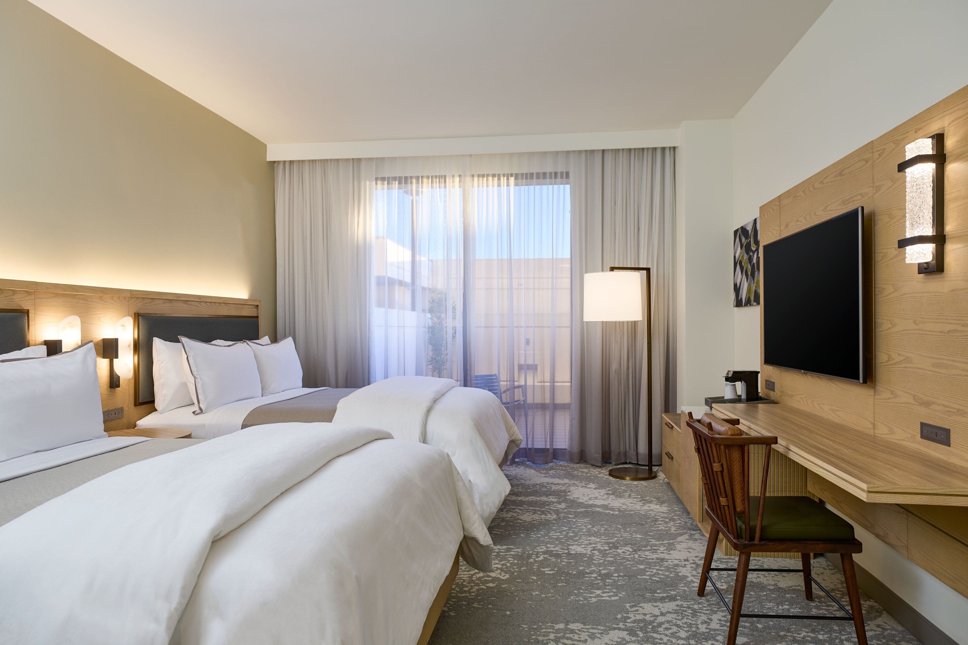 A hotel room with two beds, a TV, a desk, and a chair.