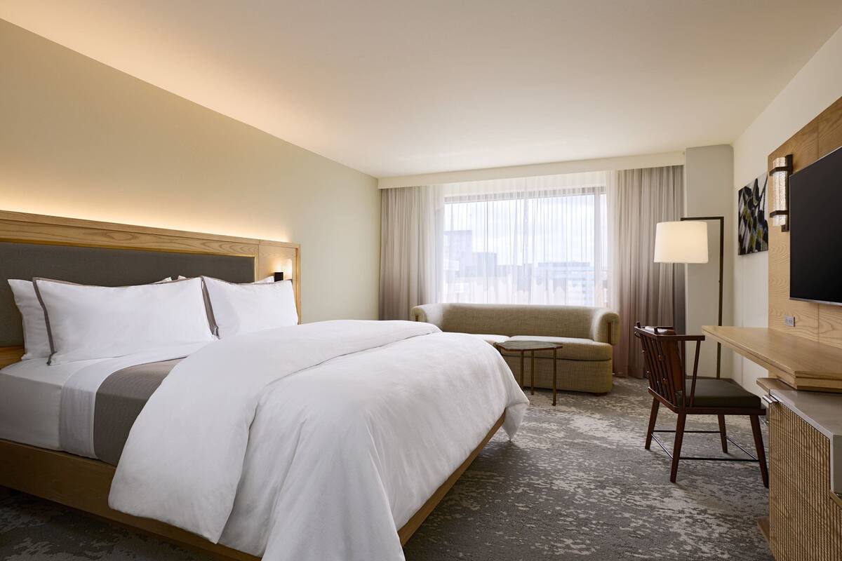 Una habitación de hotel con una cama grande, un escritorio, una silla, un televisor y una ventana con cortinas.