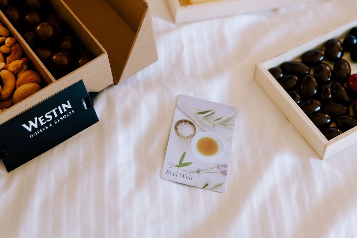 A bed with a white sheet, a box of chocolates, a box of cookies, and a card with a tea cup illustration.