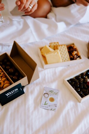 Una cama con sábana blanca, una caja de bombones, una caja de galletas y una tarjeta con una ilustración de una taza de té.
