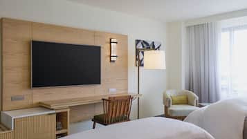 A hotel room with a flat-screen TV, a desk with a chair, a lamp, and a bed.
