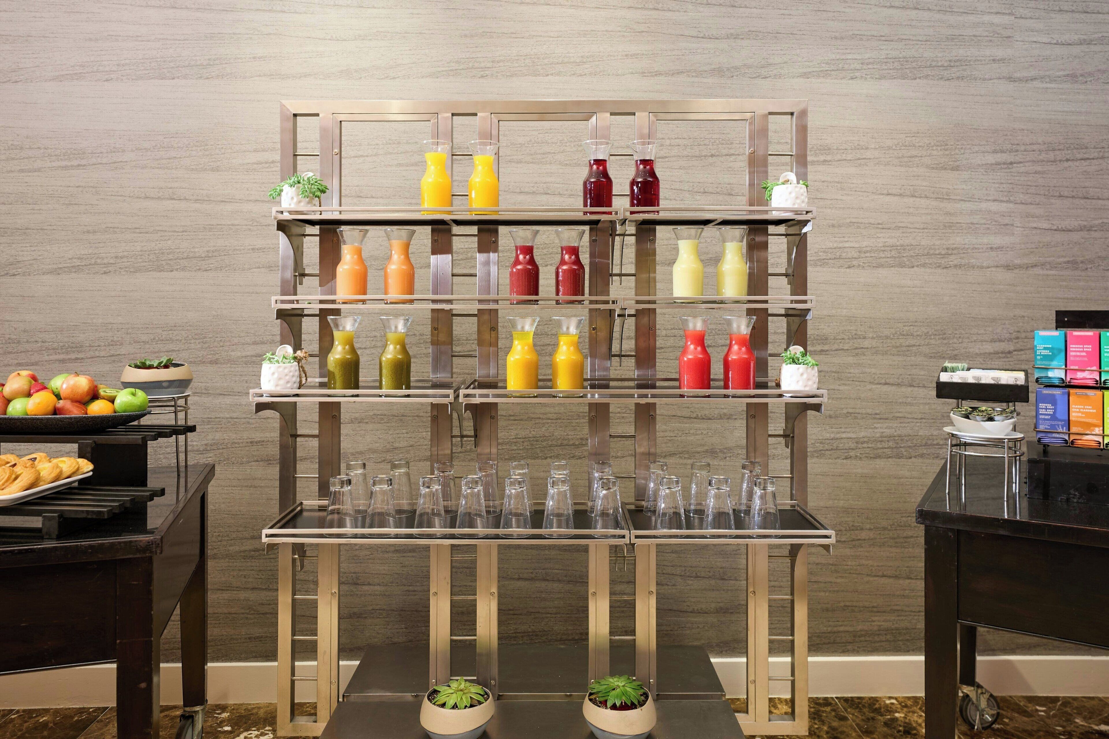 A multi-tiered beverage dispenser with various colored bottles and glasses, a fruit tray, and potted plants.