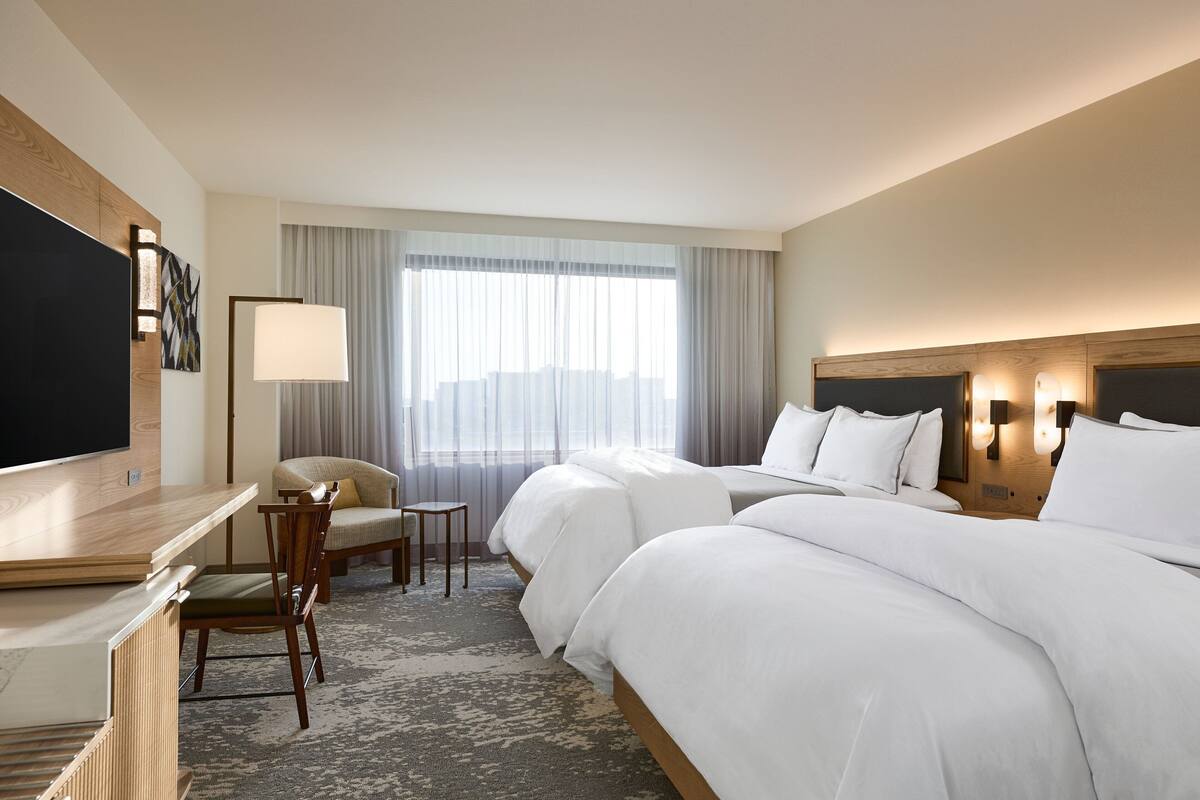 Una habitación de hotel con una cama grande, un escritorio con silla, televisor y ventana con cortinas.