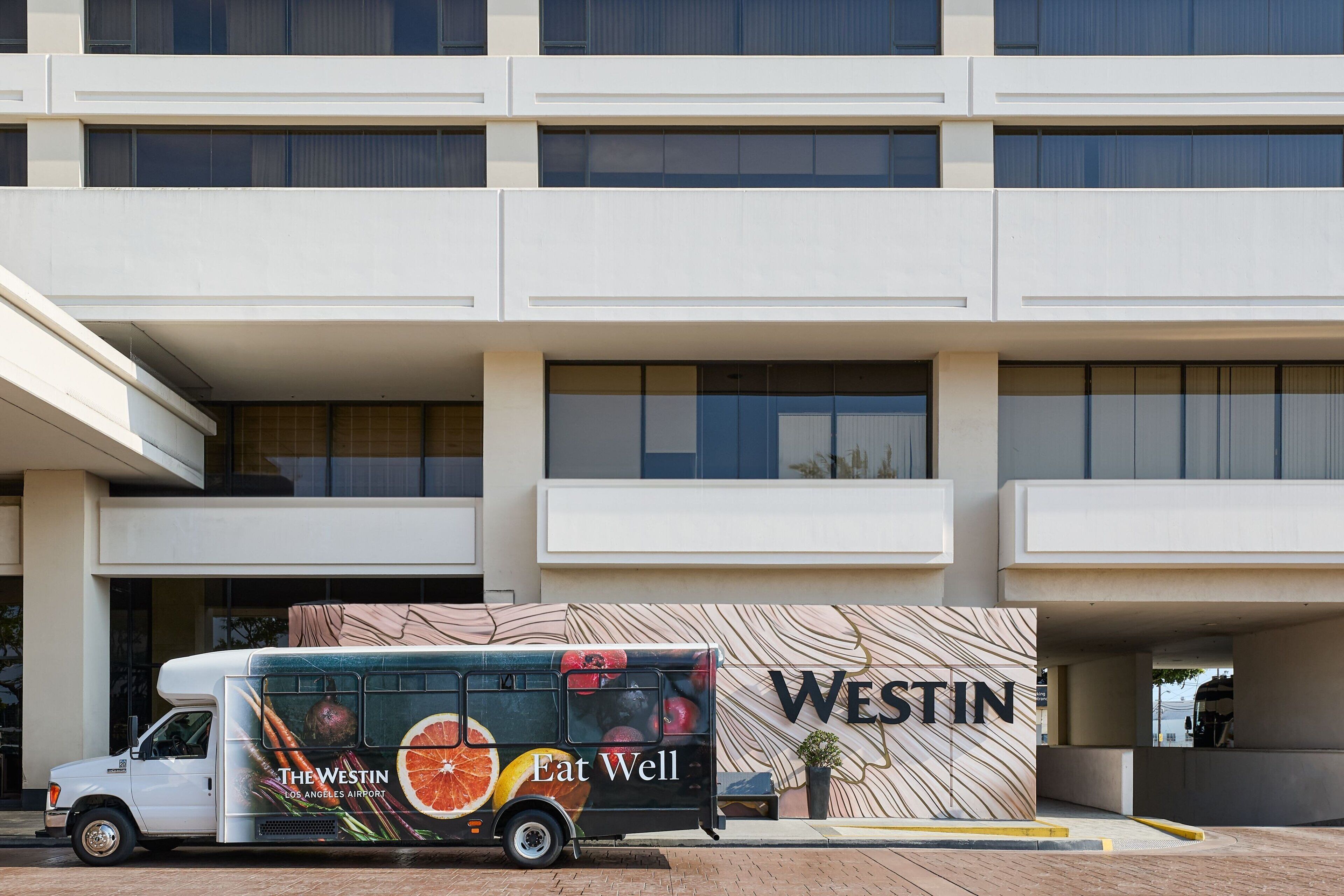 A bus with "The Westin" and "Eat Well" advertising parked in front of a hotel.