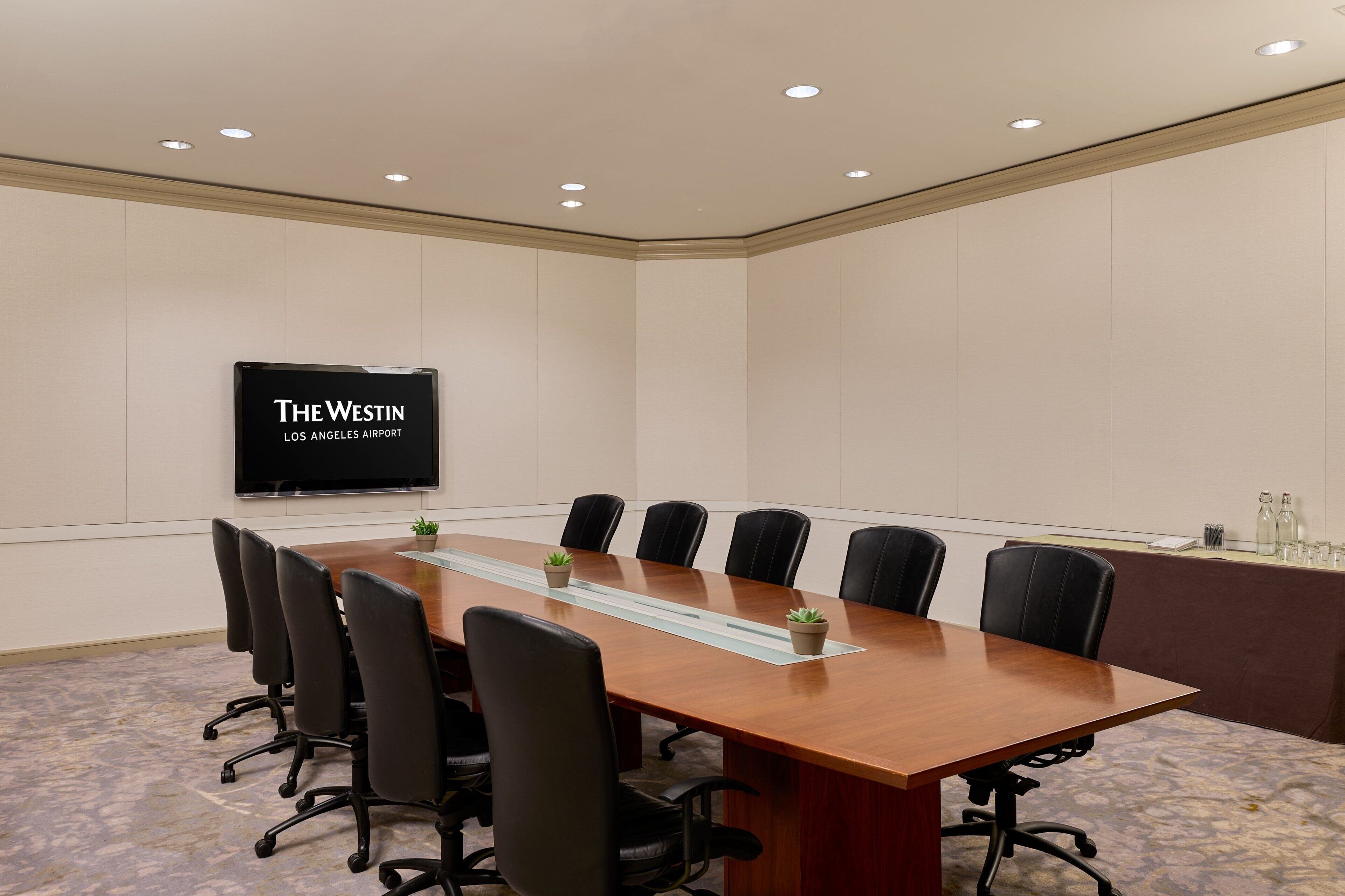 A conference room with a long table, black chairs, a flat-screen TV, and a sign reading 'The Westin Los Angeles Airport'.
