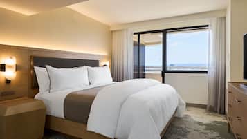 A hotel room with a large bed, a nightstand, a dresser, and a window with a city view.