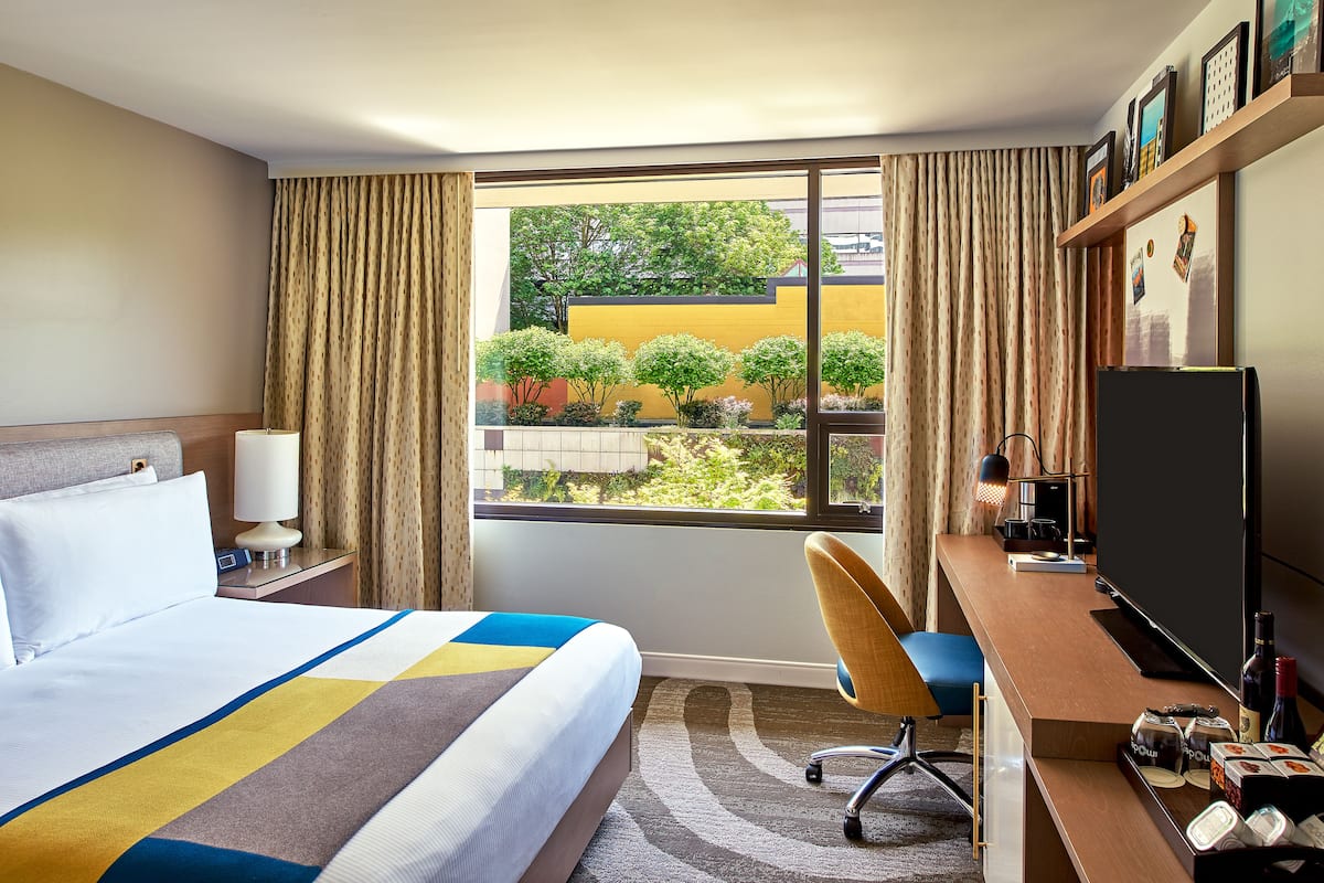 A hotel room with a large bed, a desk with a computer, a TV, and a window with curtains.