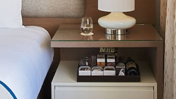Habitación de hotel con cama, mesita de noche con lámpara, vaso de agua y minibar.