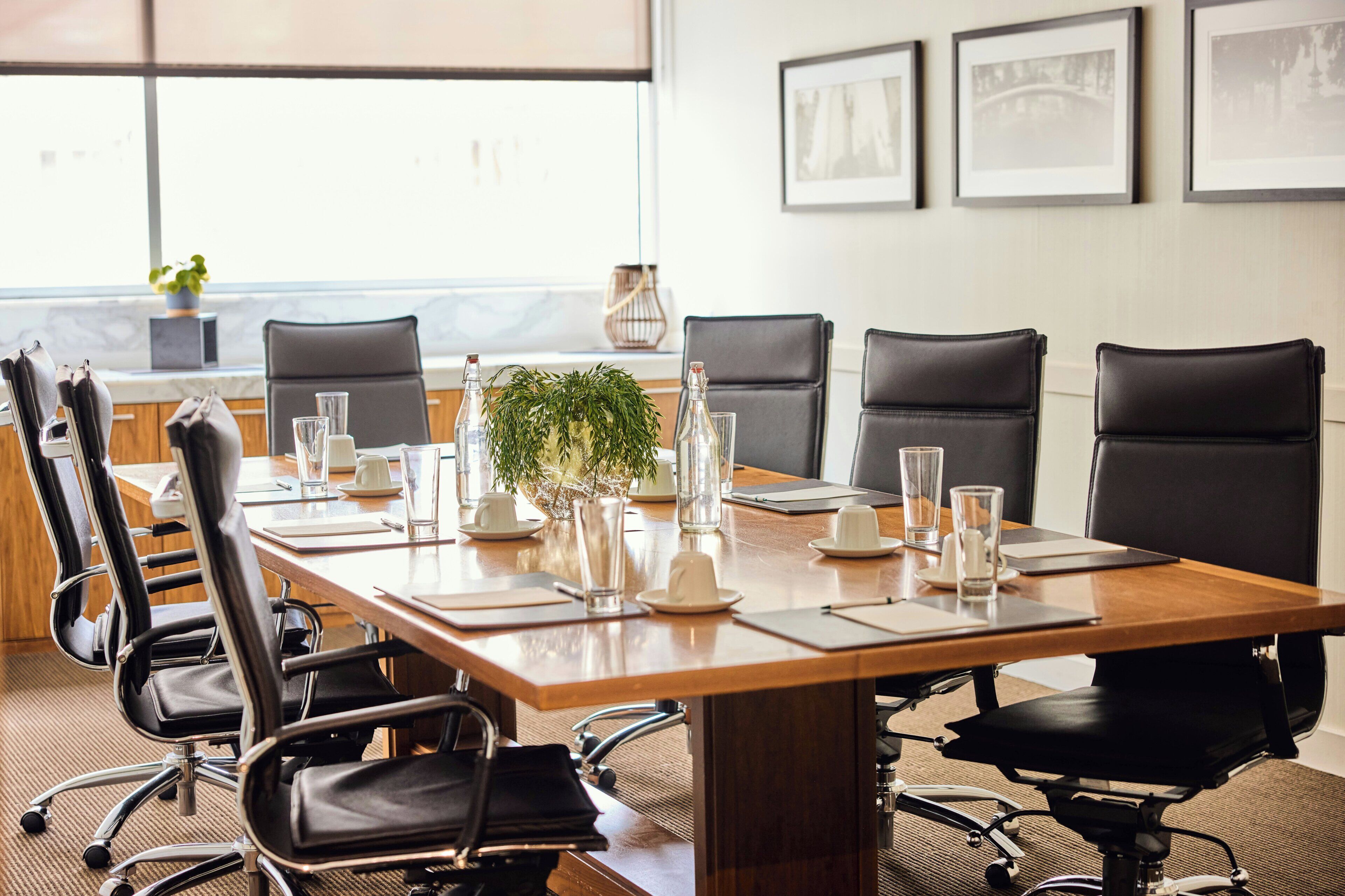A conference room with a long table, black chairs, glassware, and framed pictures on the wall.