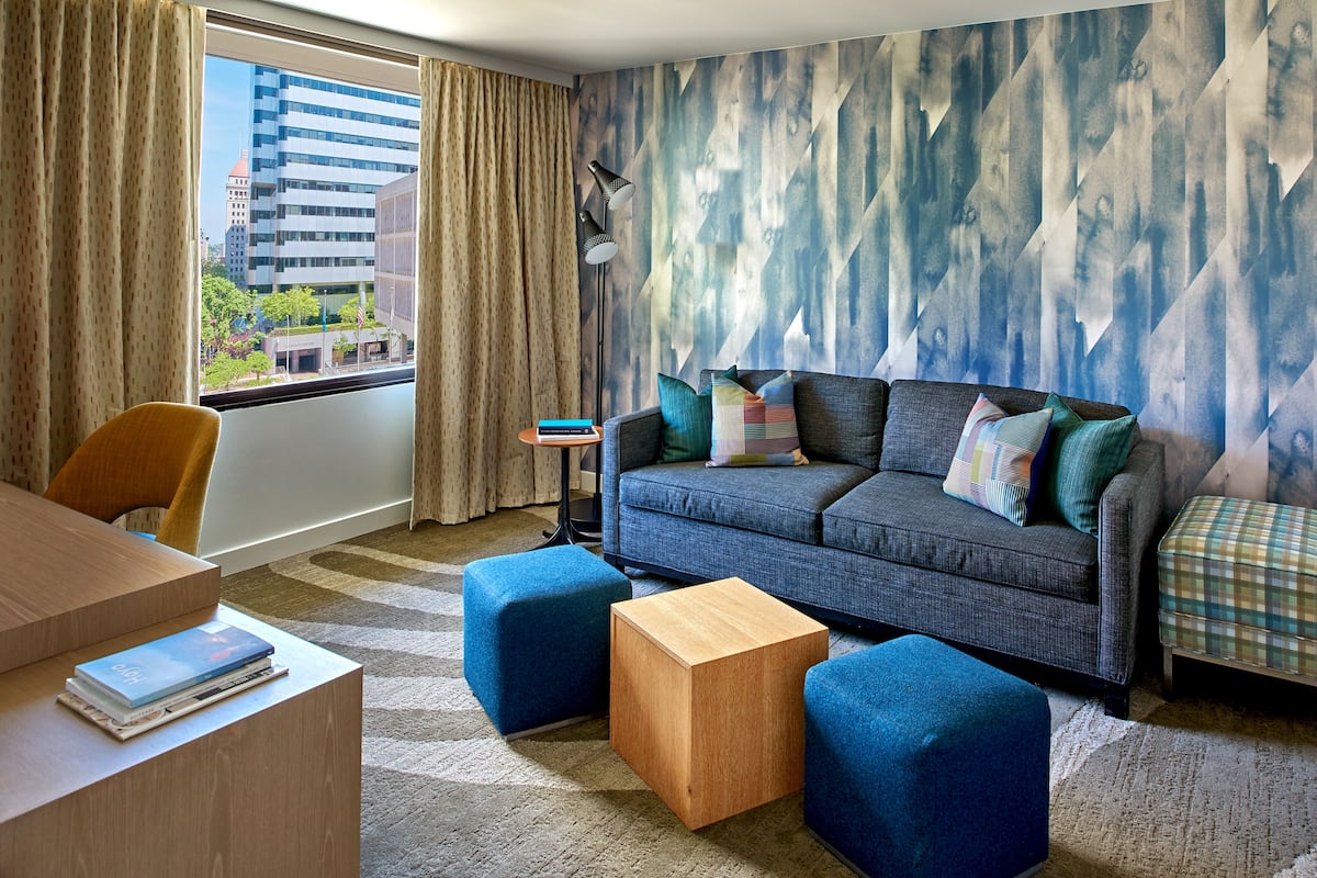 A modern living room with a sofa, ottomans, a coffee table, and a view of a cityscape through a window.
