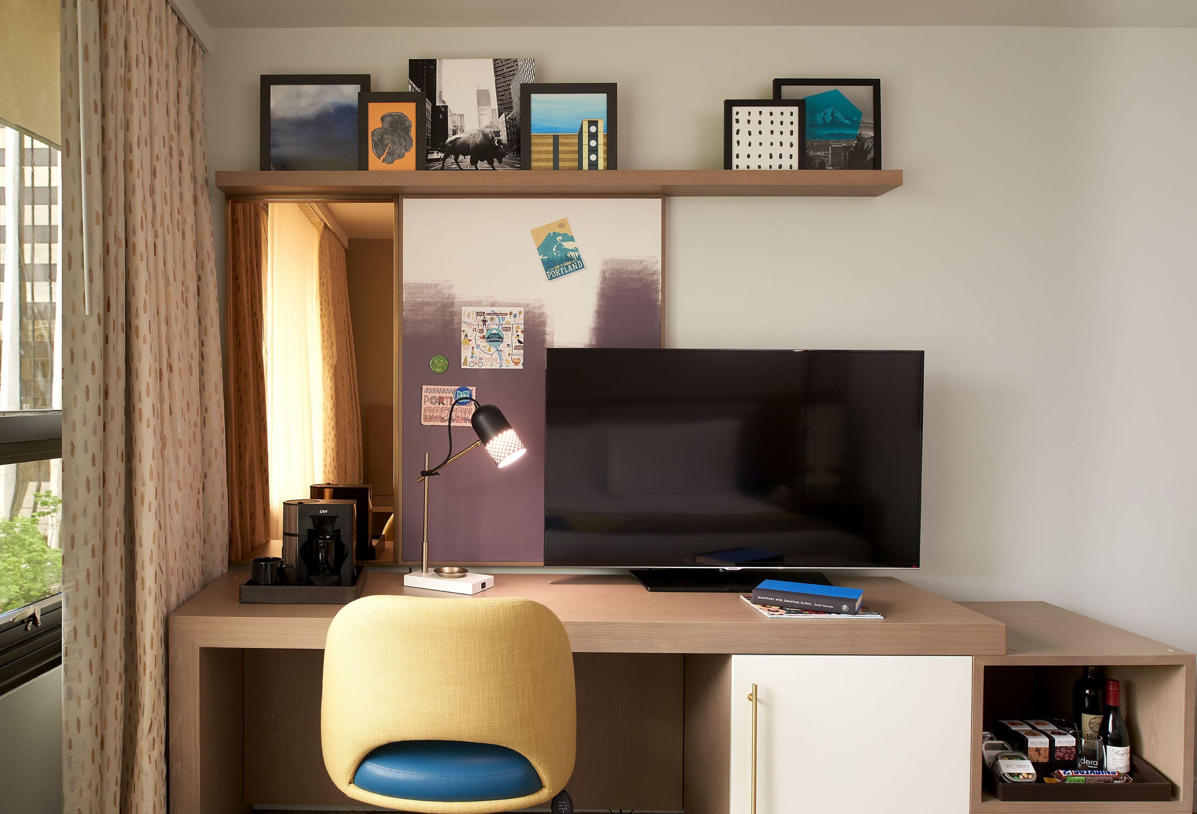 Ein moderner Schreibtisch mit einem Flachbildfernseher, einer Kaffeemaschine und einer Lampe.