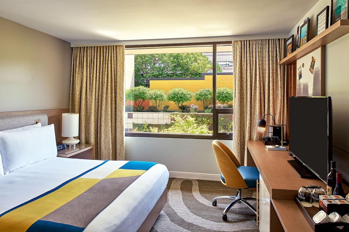A hotel room with a bed, desk, chair, TV, and a window with curtains.
