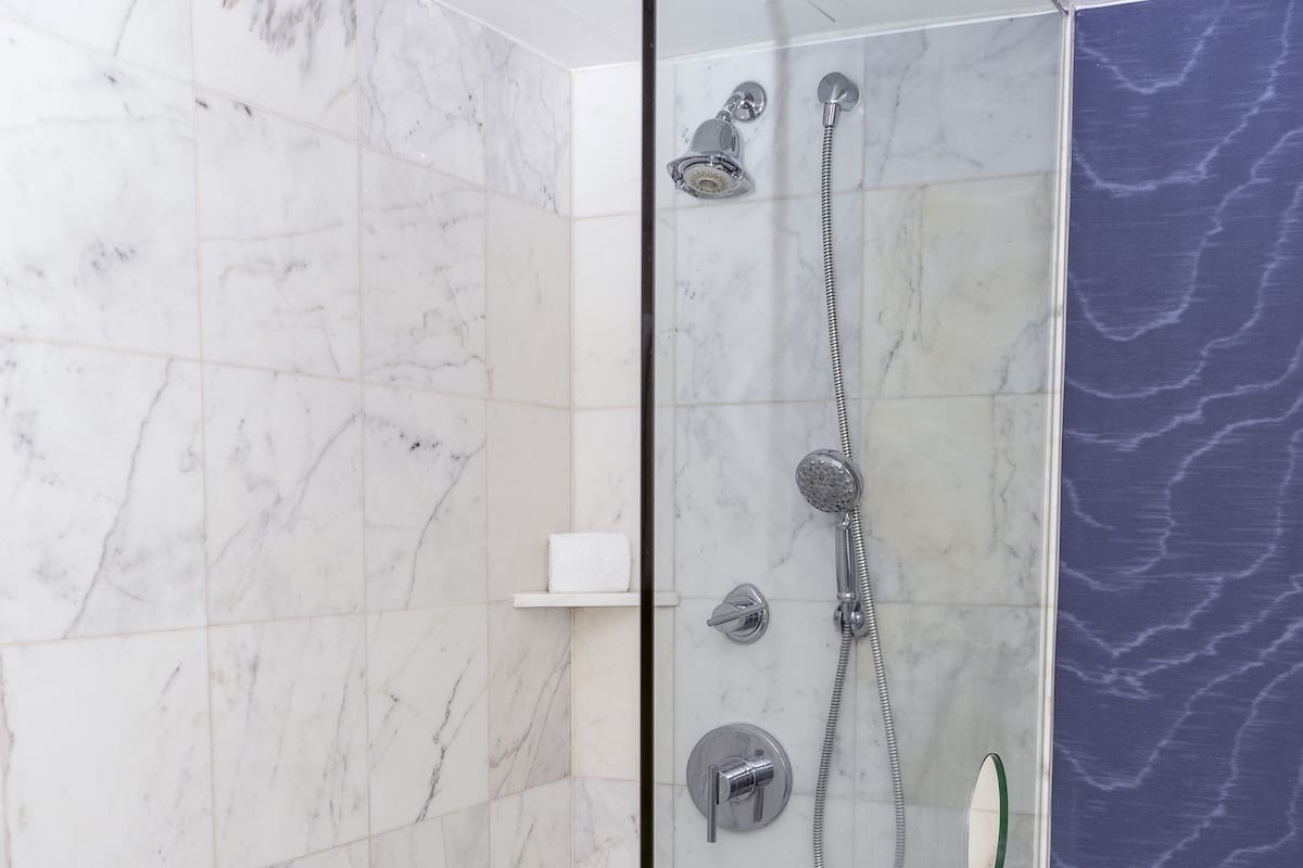 A glass-enclosed shower with a handheld showerhead, a wall-mounted faucet, and a handheld showerhead.
