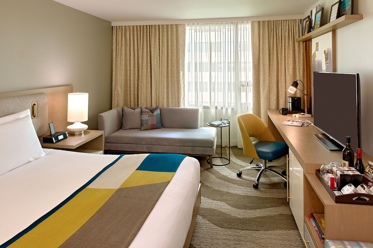 A hotel room with a bed, a sofa, a desk with a computer, a chair, and a TV.