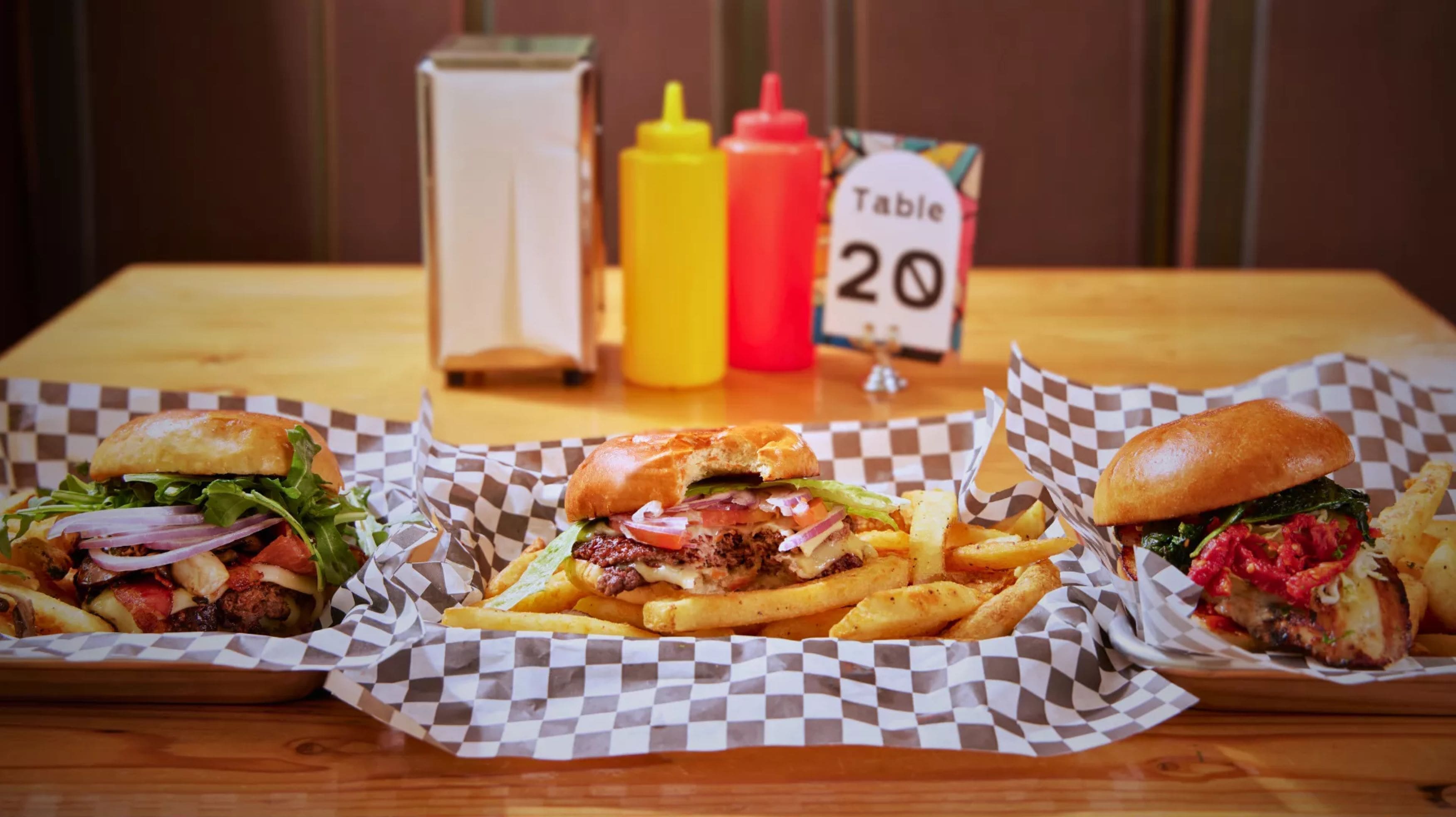 Three burgers and fries on a table with condiments and a table number.