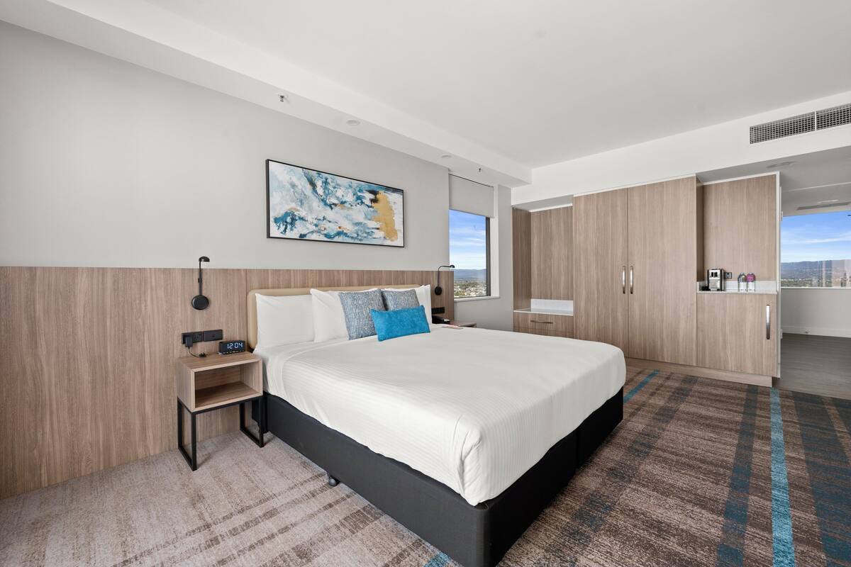 A modern hotel room with a large bed, a nightstand, a wardrobe, and a city view.