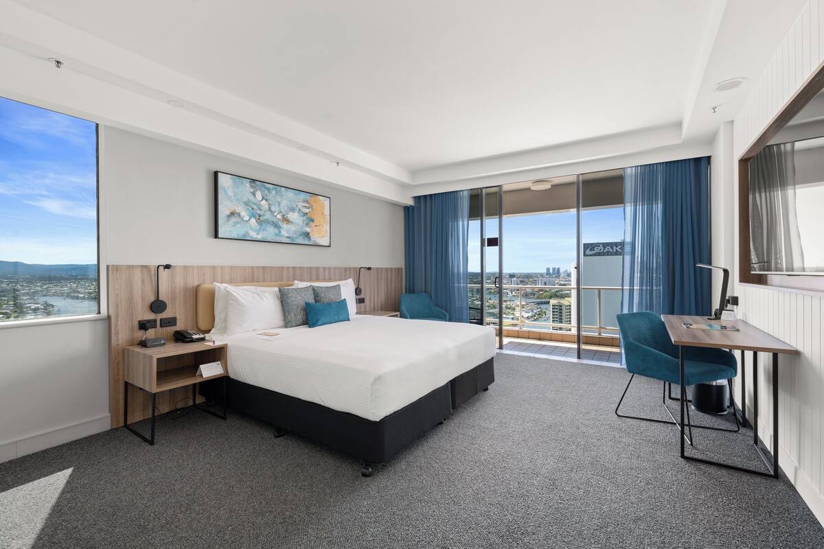 A modern hotel room with a large bed, a desk, and a view of the city.