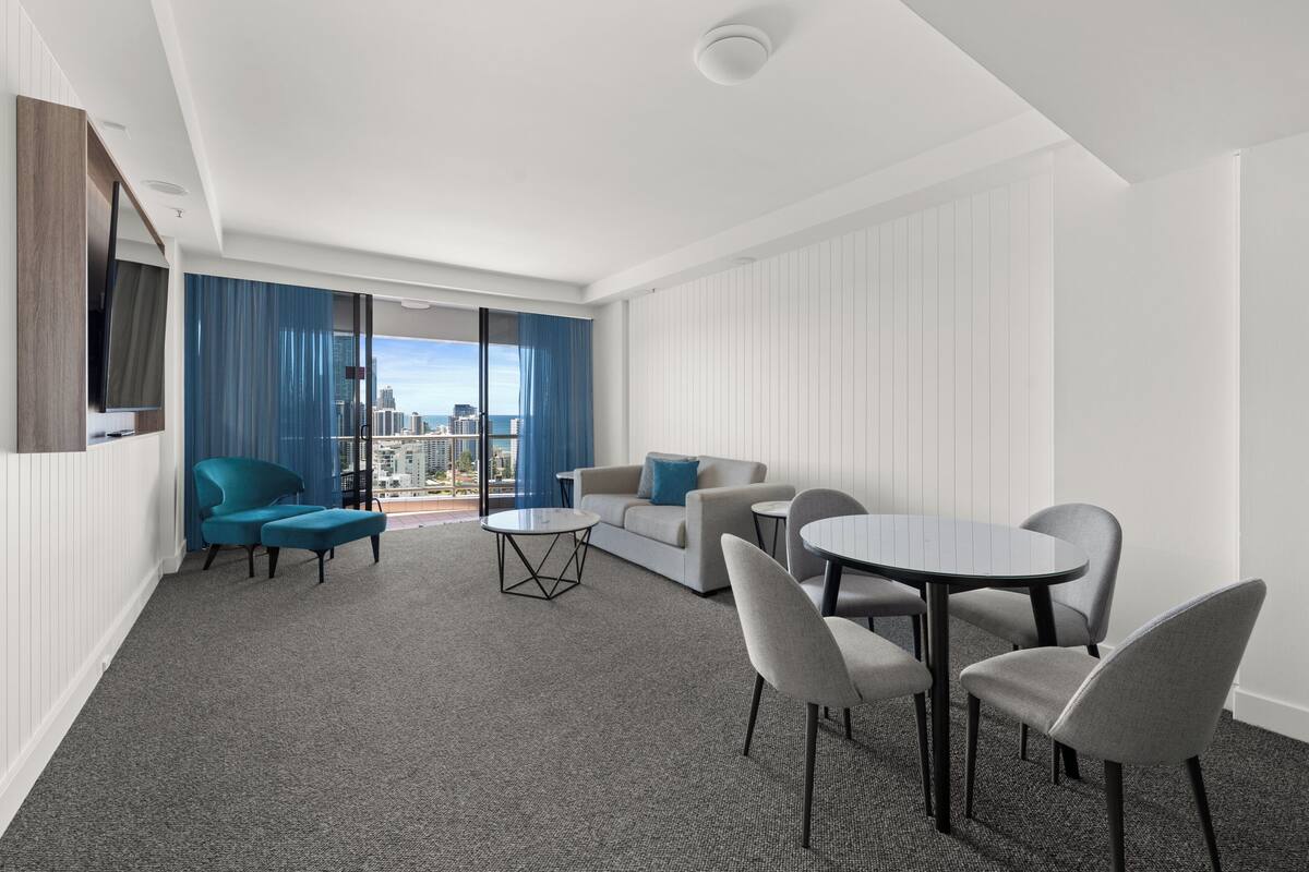 A modern hotel room with a balcony, a sofa, a dining table, and two chairs.