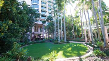 A hotel with a lush garden, palm trees, and a well-maintained lawn.