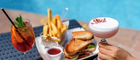 Une table dressée avec une assiette de frites, un sandwich et un cocktail.