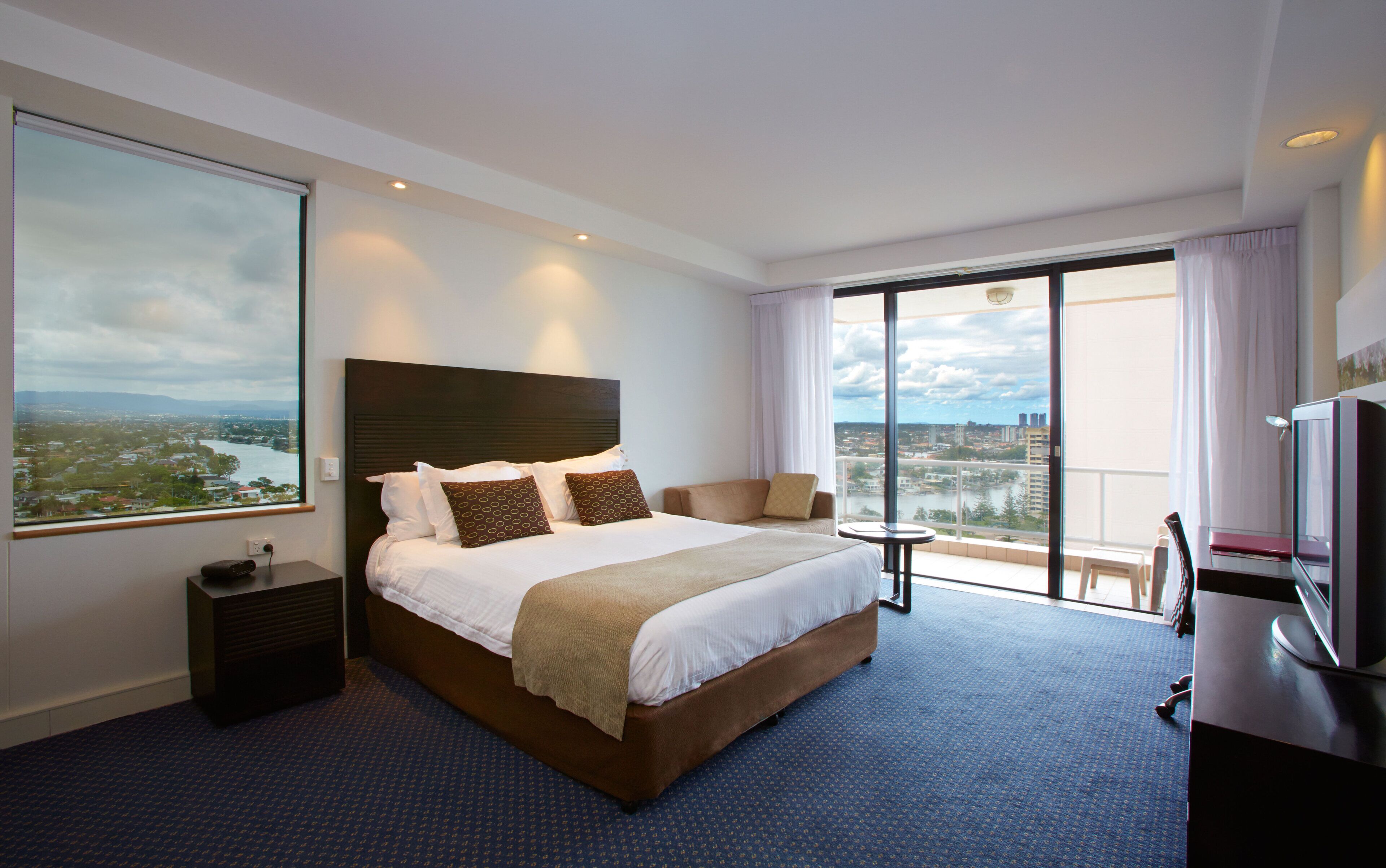 A hotel room with a large bed, a TV, a desk, and a view of a cityscape.