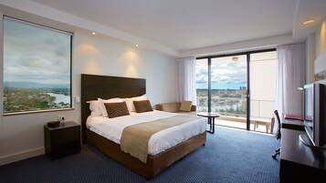 A hotel room with a large bed, a TV, a desk, and a view of a cityscape.