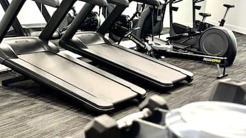Un gimnasio con cintas de correr, bicicletas estáticas y mancuernas.