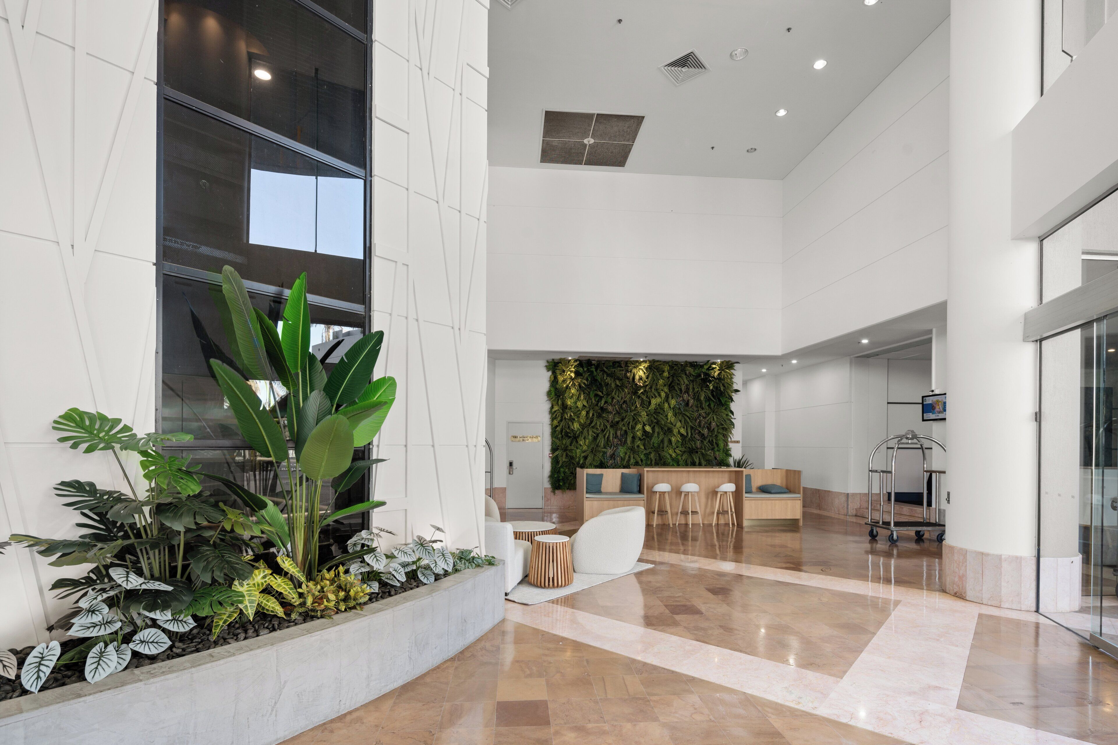 Un hall d’entrée spacieux comprenant un comptoir d’accueil, un espace détente et un grand bac à plantes contenant diverses espèces végétales.