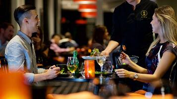 A restaurant setting with diners at tables, a waiter serving food, and a candle on the table.
