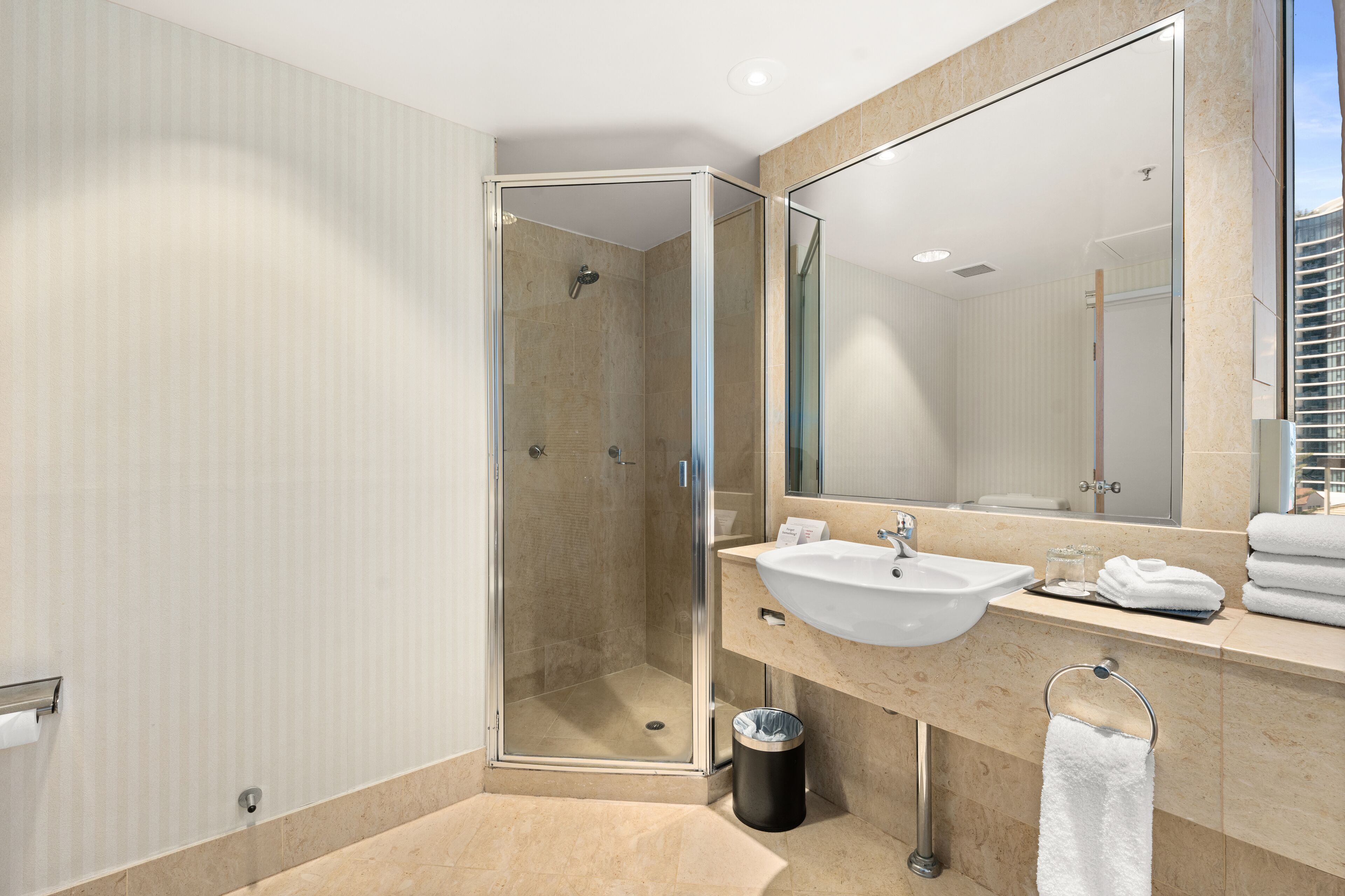 A modern bathroom with a glass-enclosed shower, a sink, and a large mirror.