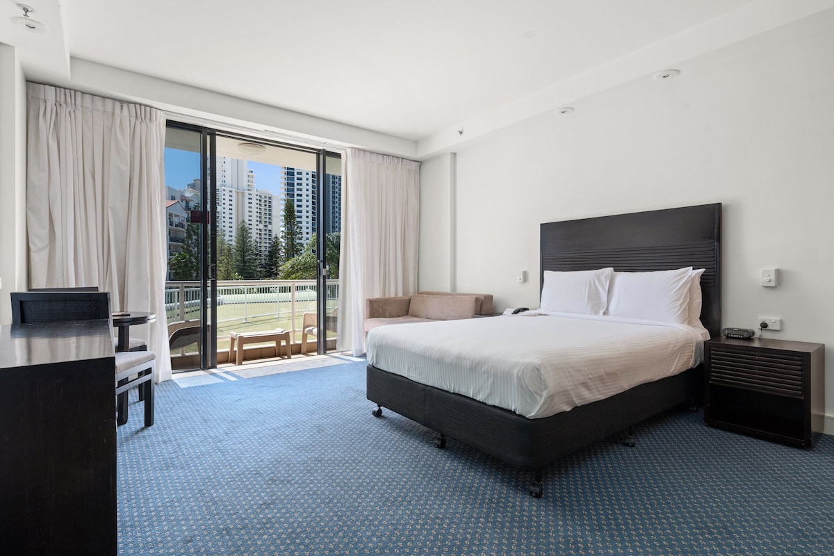 Una camera d'hotel con un letto grande, una scrivania, una sedia e un balcone con vista sui grattacieli.